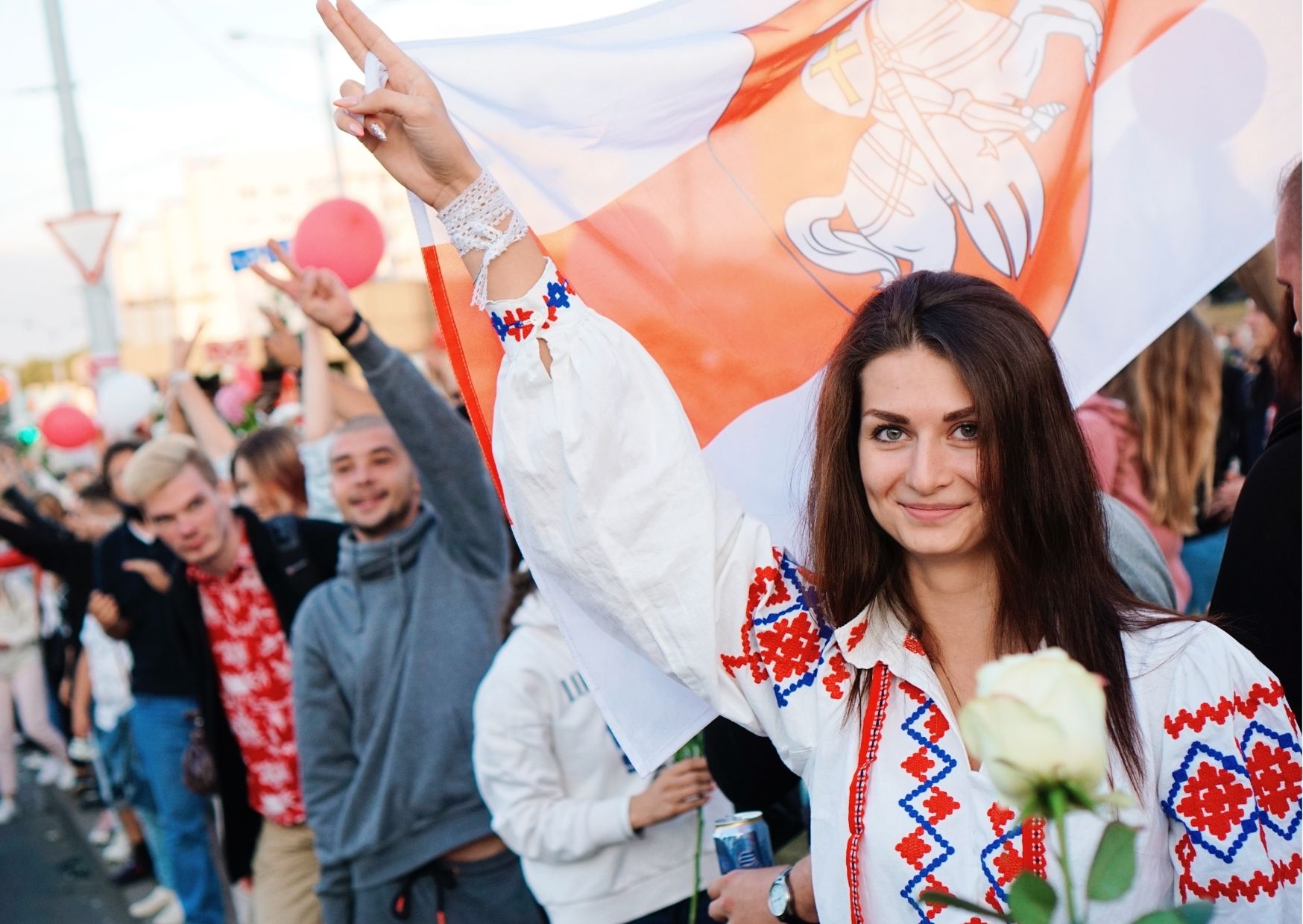 A woman in traditional belarus costume stands in front of a flag