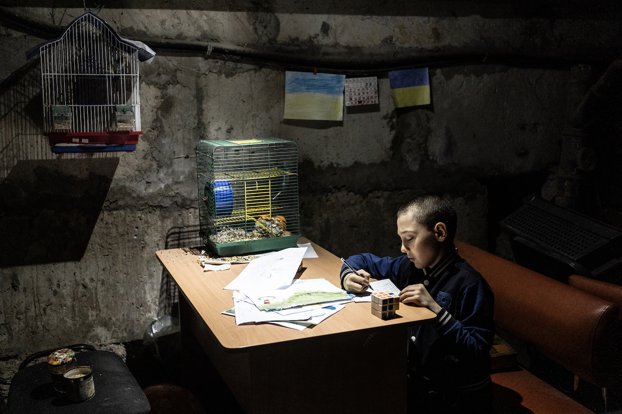 A boy sits in the dark room under some lights and paints 