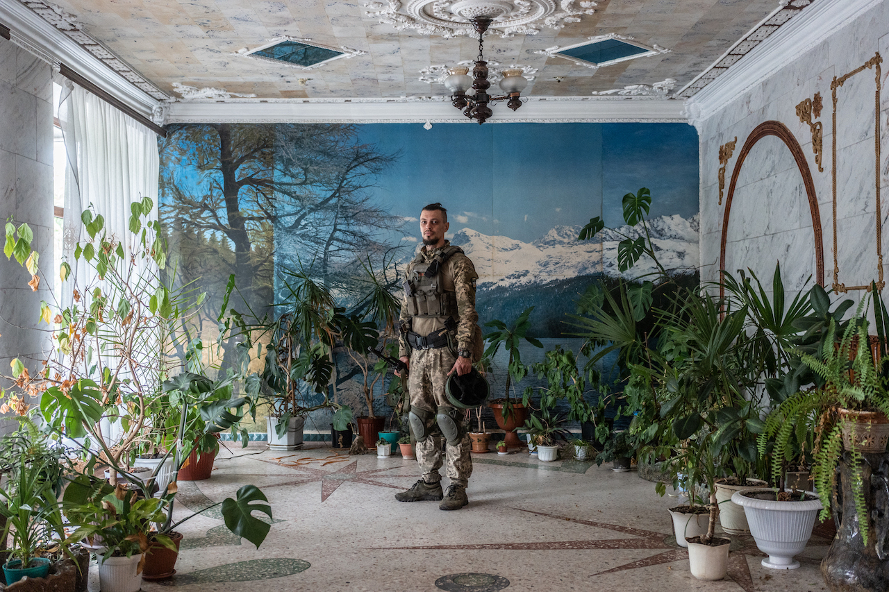 Ukrainian soldier stands in a room full with potted flowers 