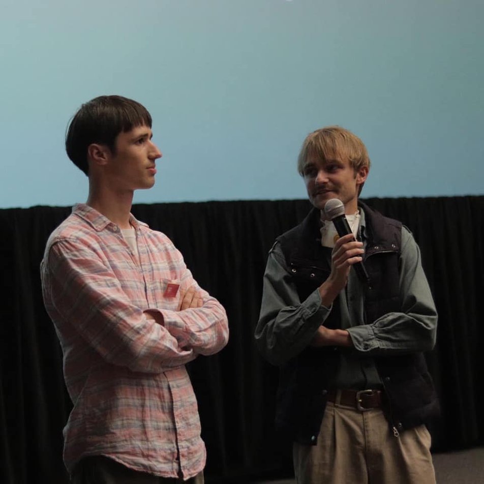 Two men are on the stage, one of them holds a microphone