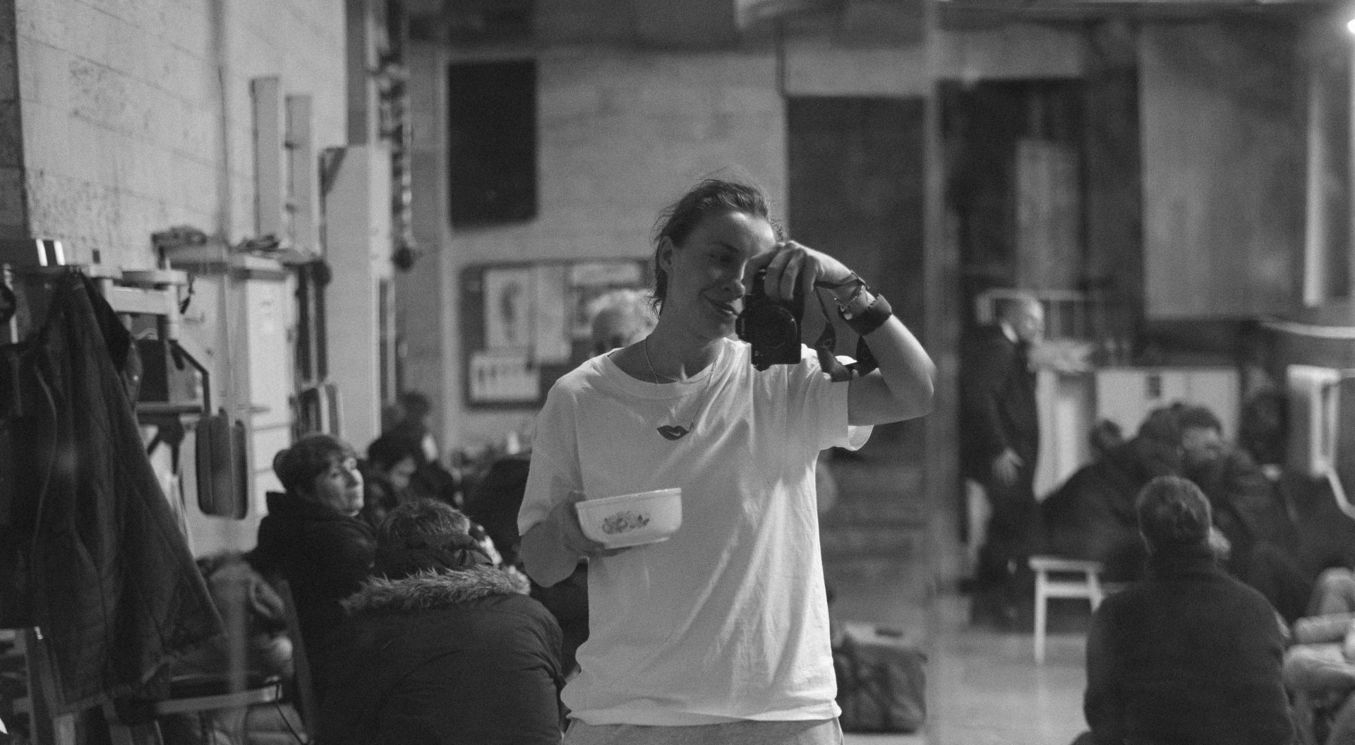 A woman stands with a camera depicting herself, black and white 