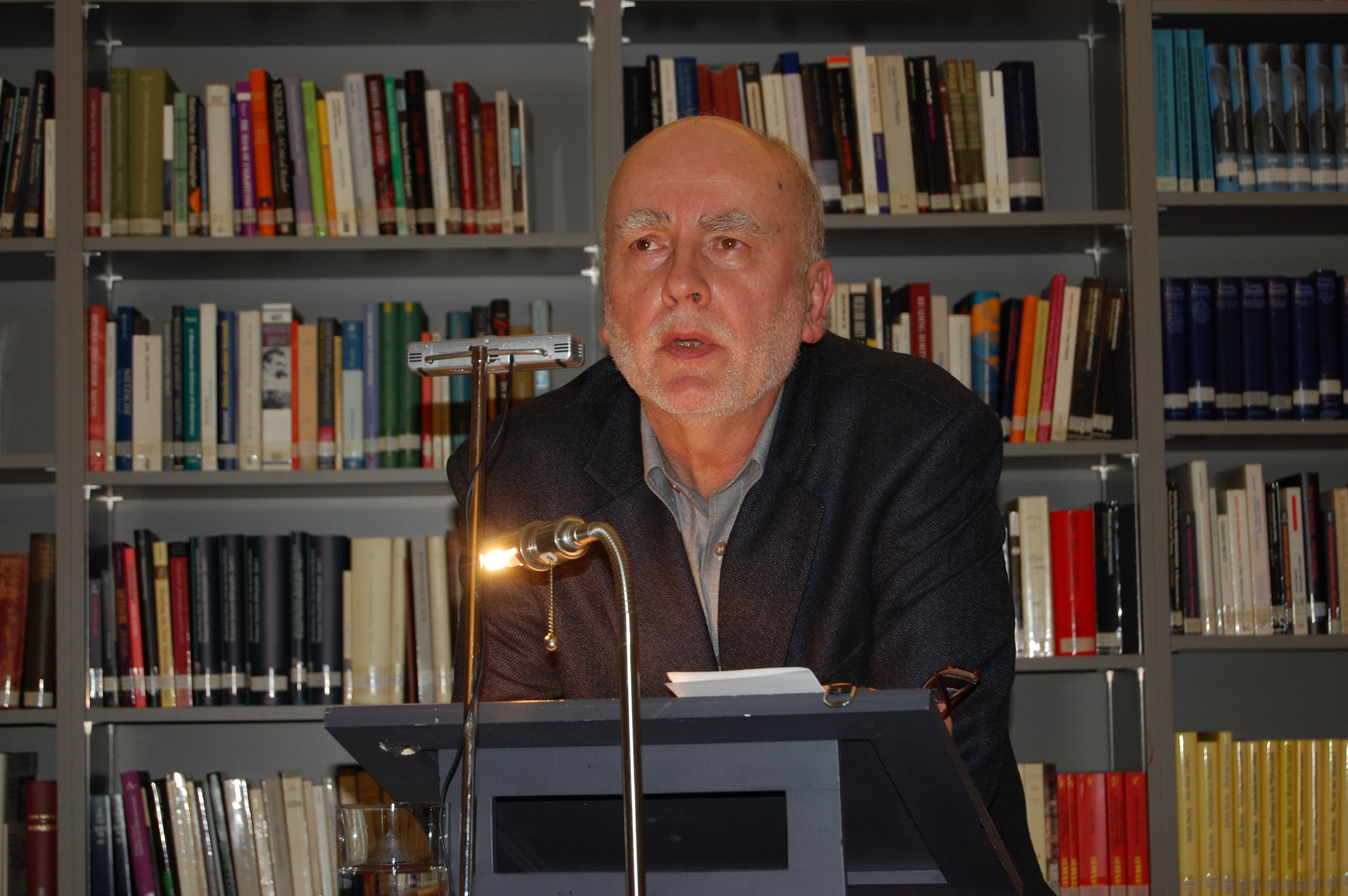 Adam Zagajewski in front of book shelves in the IWM library giving a talk