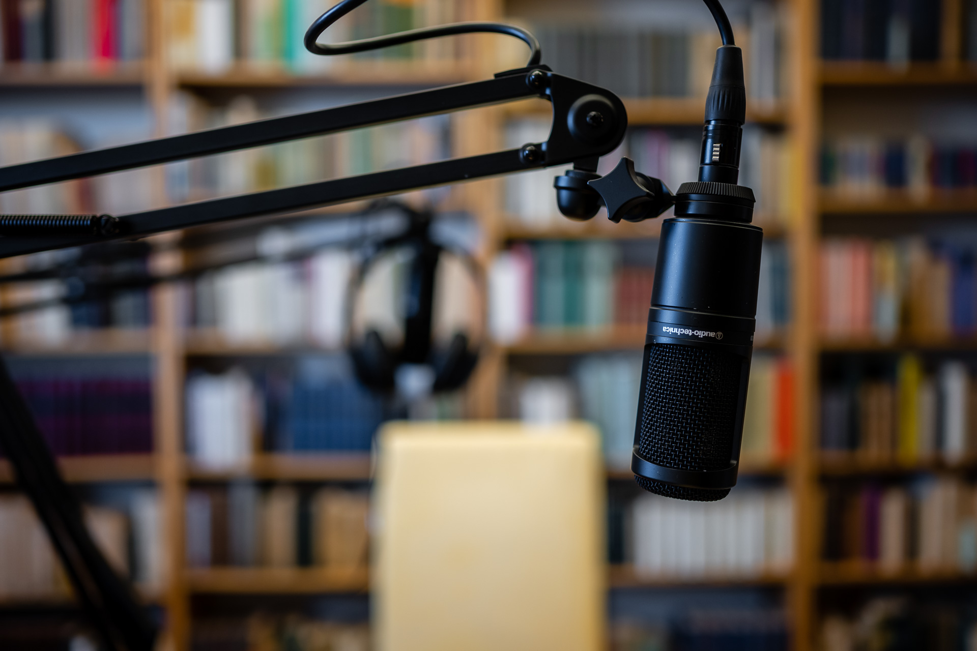 Podcast recording equipment at the IWM in front of a wall of books. A microphone in the foreground and blurry headphones in the background.