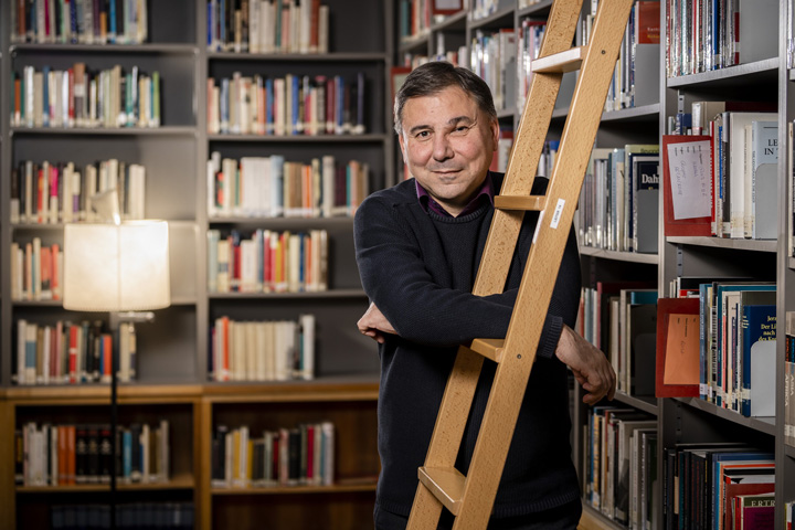 Ivan leaning on the ladder in the IWM library with books in the background