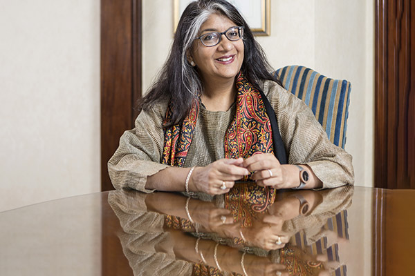 Shalini Randeria wearing a brown shawl sits at a table smiling