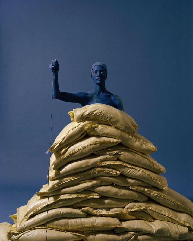 A person colored in blue in front of a blue background with bags in front of her hiding her body 