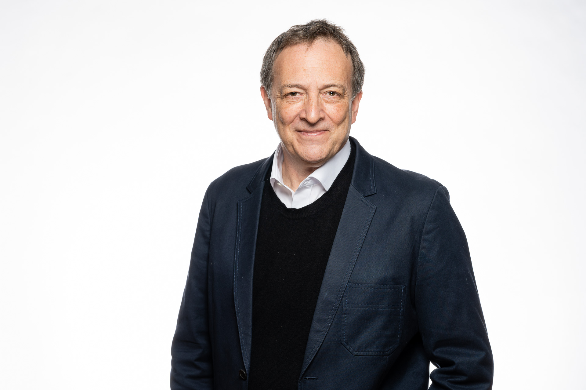 Misha Glenny headshot. Wearing a white shirt with a dark blue sweater and blazer.