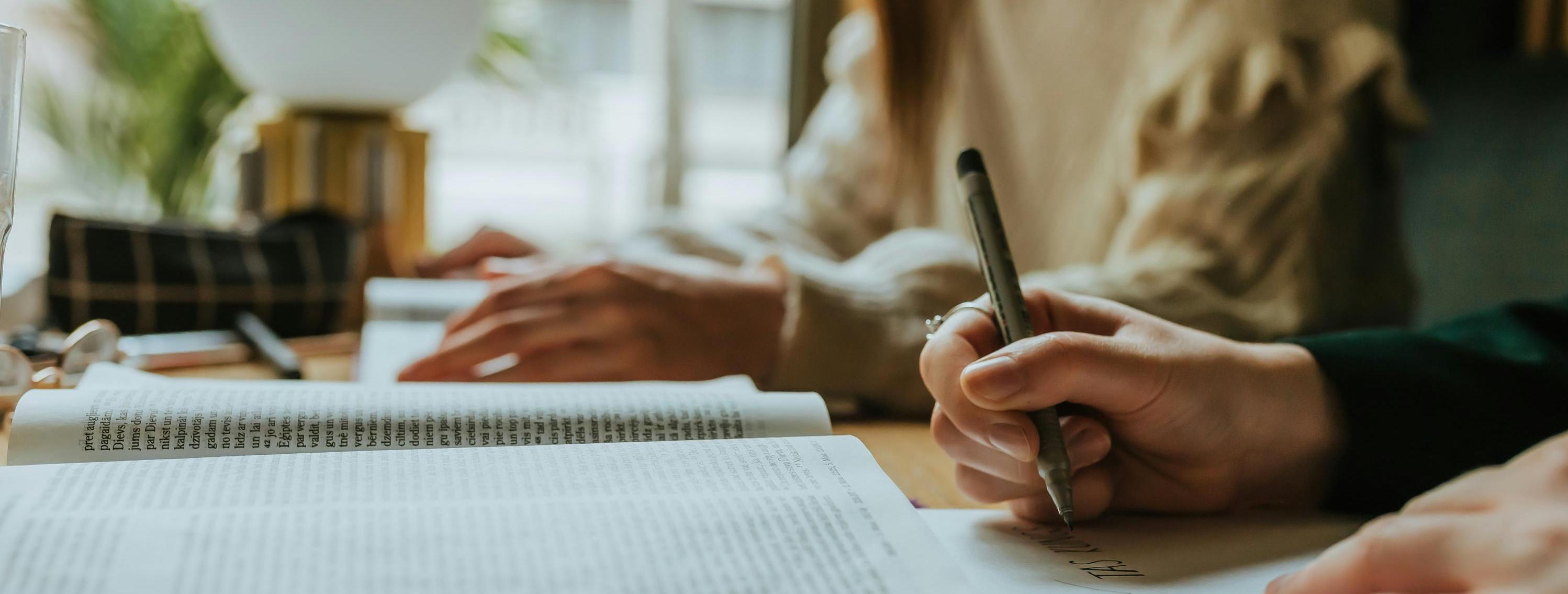 Two hands and a book with one person writing into a booklet