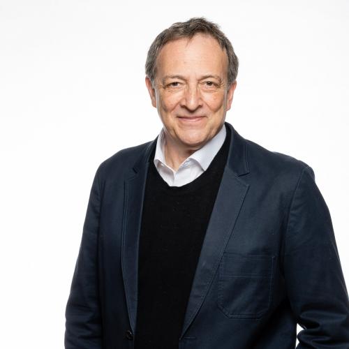 Misha Glenny headshot. Wearing a white shirt with a dark blue sweater and blazer.