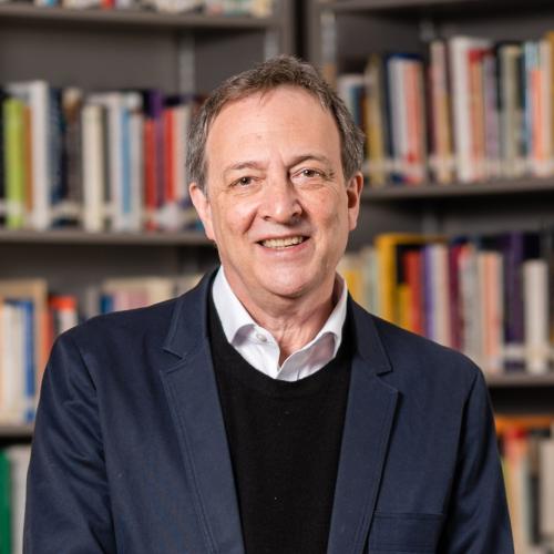Misha Glenny headshot. Wearing a white shirt with a dark blue sweater and blazer.